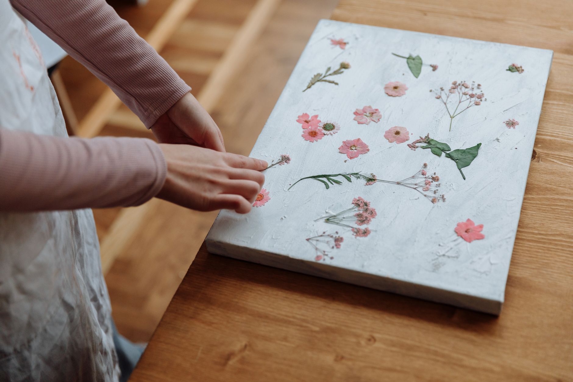 Hands arranging pressed flowers on a canvas