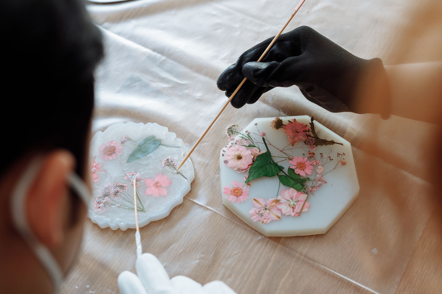 Gloved hands arranging dried flowers in a resin mold