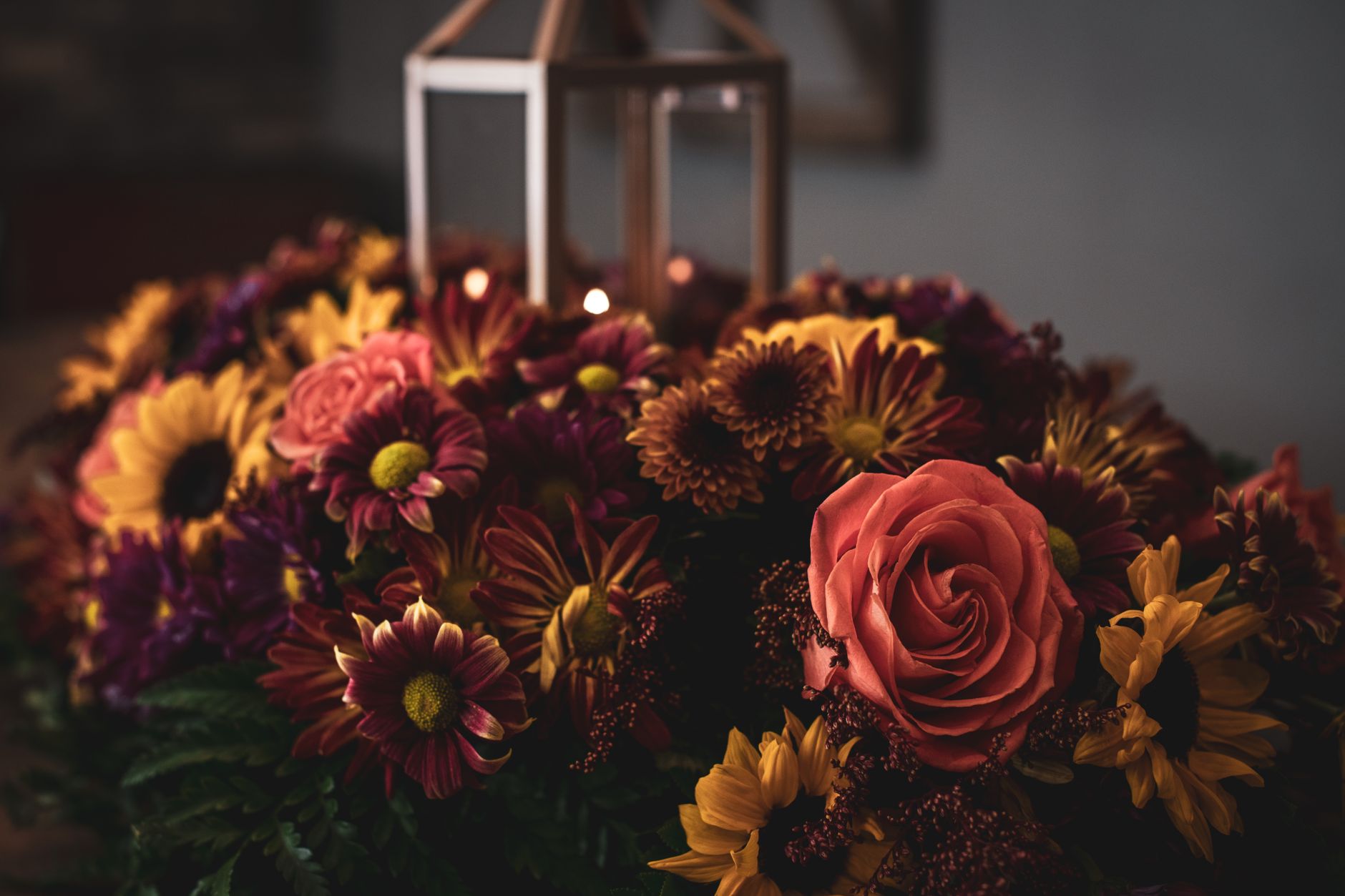 Autumn floral arrangement with chrysanthemums and roses beside a decorative lantern