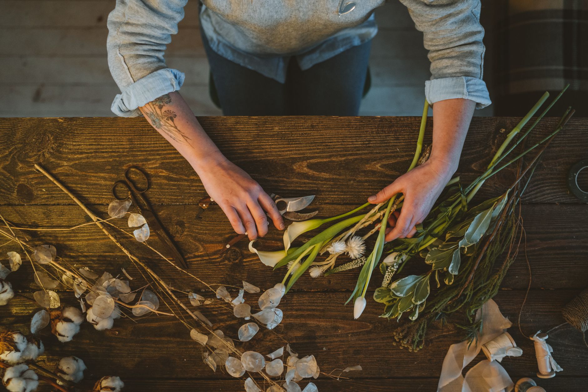 Hands arranging white and green flowers on a wooden table