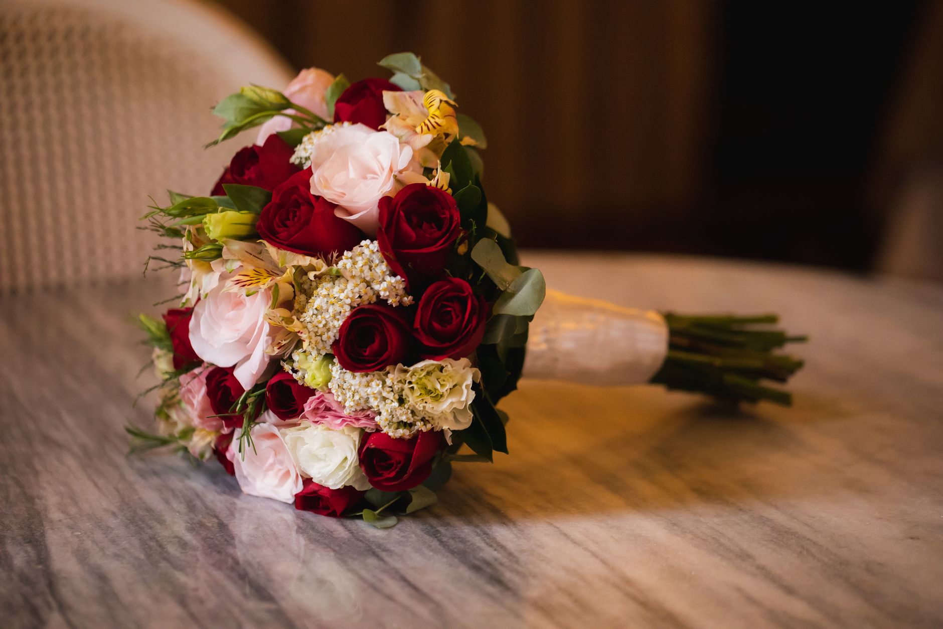 Bridal bouquet of red and pink roses with greenery on a marble table